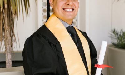 a man wearing black toga holding rolled certificate while smiling at the camera